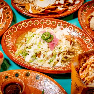 Different dishes placed on a table, plate of taquitos in the focus.