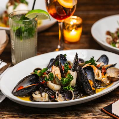 A plate of steamed mussels with fennel, served with an Aperol Spritz and a Mojito.