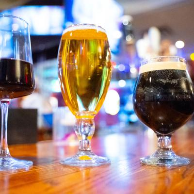 Three glasses on a bar counter: red wine, golden beer, and dark stout.