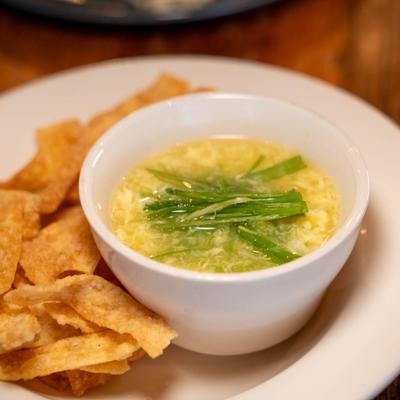 A bowl of clear yellow broth with green onions next to a pile of crispy tortilla chips.