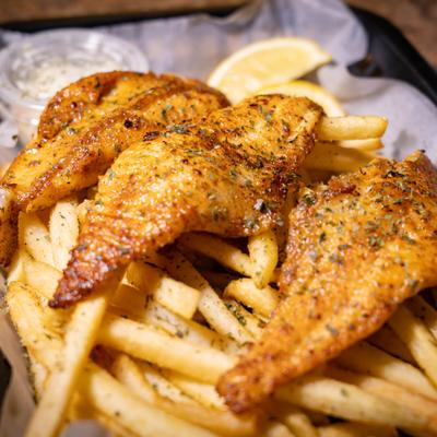 Grilled catfish with herb seasoning, fries, and lemon wedge.