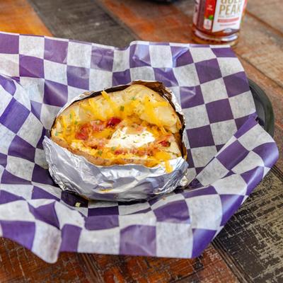Loaded baked potato served in a purple and white checkered paper liner.