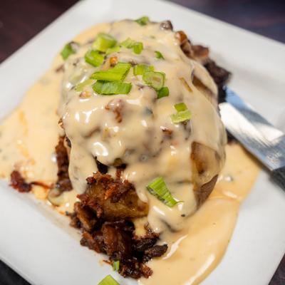 Loaded baked potato topped with bacon bits, creamy sauce, and chopped scallions.