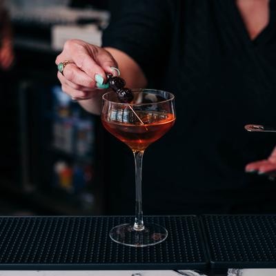 A bartender garnishes the Mn-Hattan cocktail with cherries.
