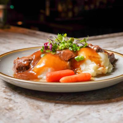 Pot roast served with mashed potatoes, garvy, baby carrots and micro greens.