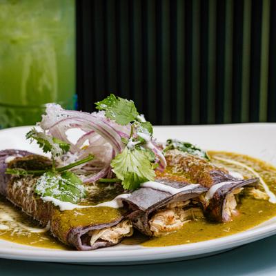 Enchiladas with green salsa, crema, drizzle, and cilantro garnish.