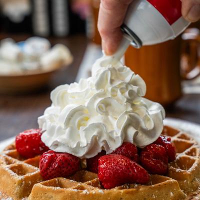 Whipped cream being sprayed onto a waffle topped with strawberries.