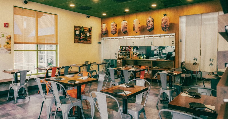 Interior, wooden tables, metal chairs, large window, hanging lanterns, and visible kitchen area
