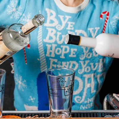 A bartender holding two liquor bottles above a tall glass.