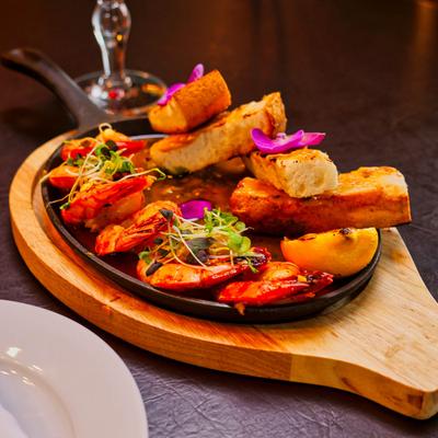 Butter-poached prawns in a white wine reduction with garlic toast, microgreens, and flower petals.