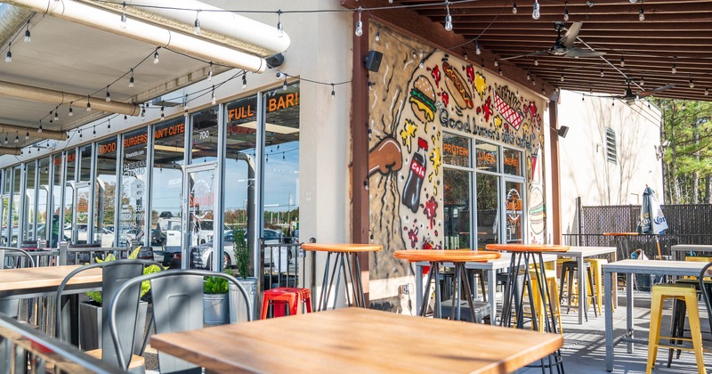 Outdoor restaurant seating area with tables, stools and a food-themed mural.