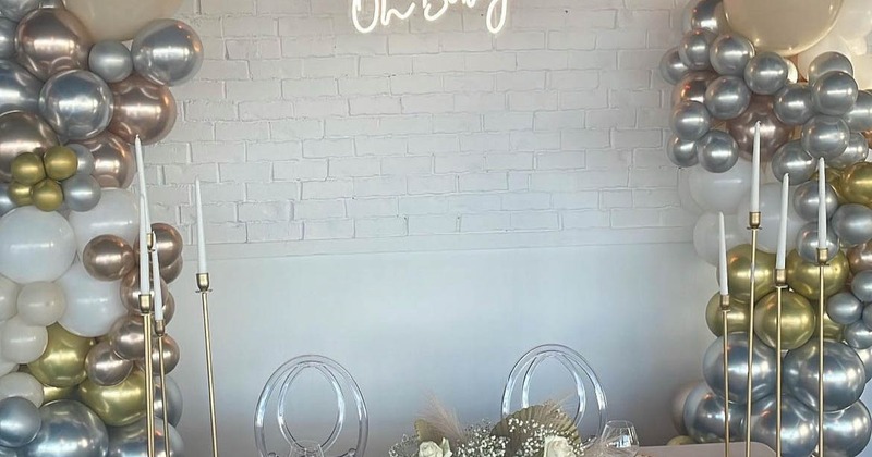 A white party table with floral decor, candles, silver, white and gold balloons