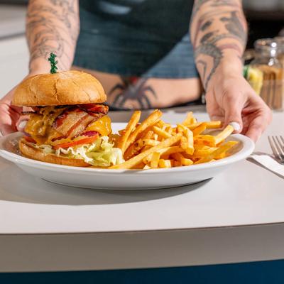 A server places a plate of classic cheeseburger and fries on a white counter.
