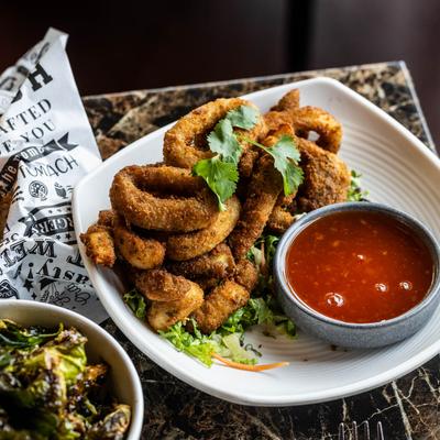 Fried Calamari served with hot, sweet and sour sauce, next to a bowl of Brussels sprouts.