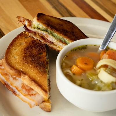 Toasted sandwich accompanied by a bowl of chicken noodle soup.