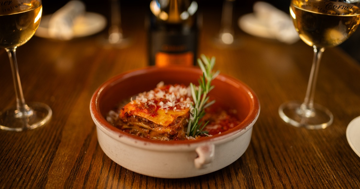Baked lasagna with marinara sauce, grated cheese, and rosemary garnish