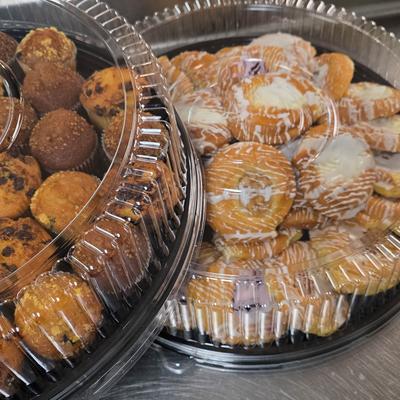 Two plastic bakery trays or containers filled with assorted baked goods.