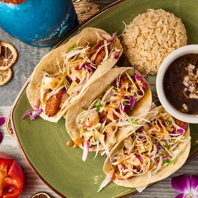 Baja tacos served on a green plate with rice and charro beans.