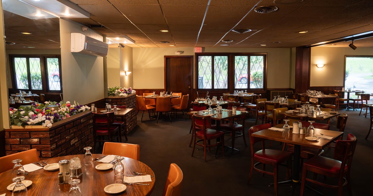 A warmly lit interior - wooden tables and chairs, decorative flowers and large windows