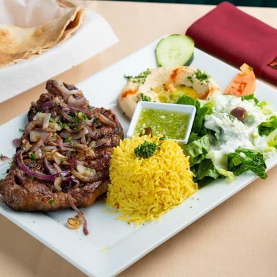 Grilled steak topped with onions served with rice, hummus, and a side salad.