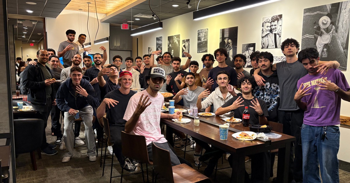 Large group of people posing inside a restaurant with pizza on the tables