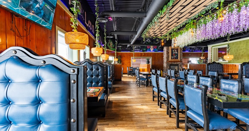 Interior, blue leather booths, wooden floors, hanging greenery, and TVs on the walls