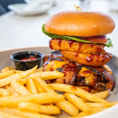 A towering bacon cheeseburger with onion rings, BBQ sauce, and golden fries.