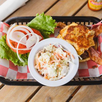 Cheeseburger with bacon served alongside coleslaw and fresh vegetables.