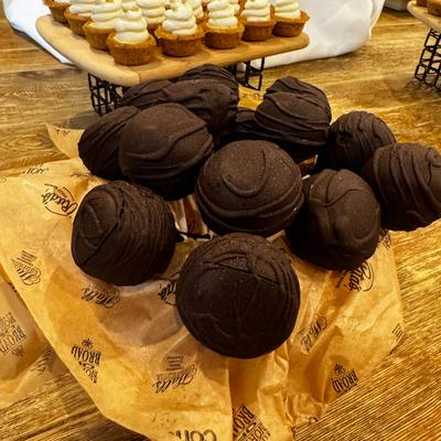 Chocolate-coated cake pops with mini cupcakes in the background.