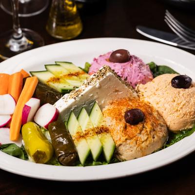 Appetizer sampler plate with grape leaves, hummus, feta cheese, and vegetables.