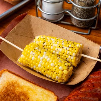 Two pieces of seasoned corn on a skewer inside a paper boat.