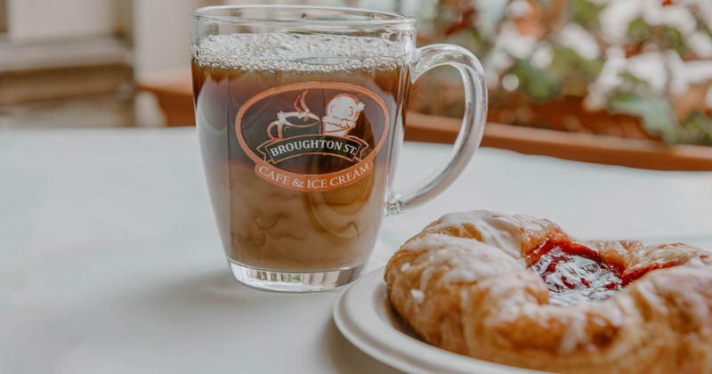 Glass mug with iced coffee and a fruit pastry on a white plate