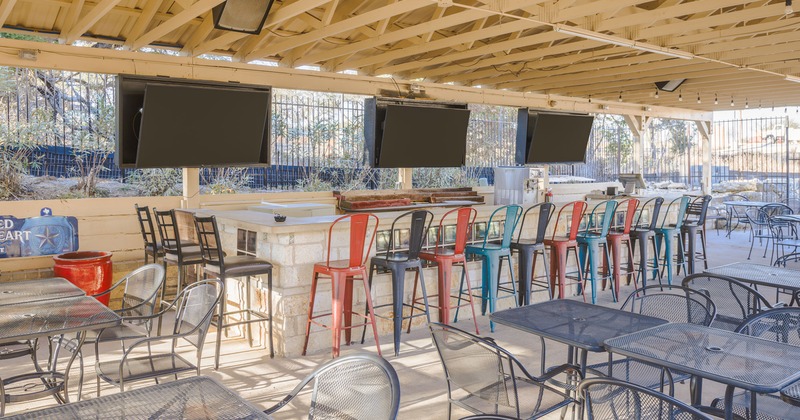 Covered patio with tables and chairs, bar and TV sets above the bar