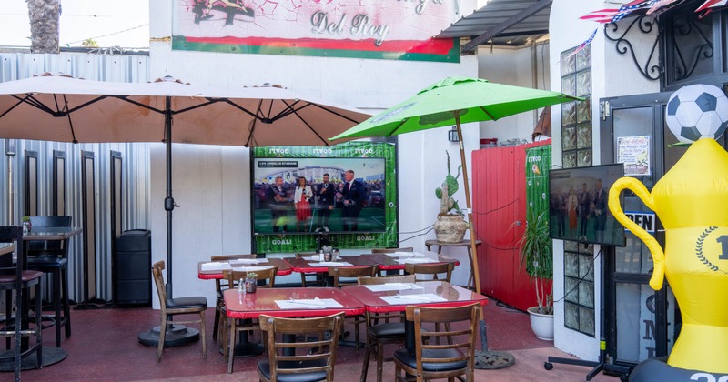 Exterior, seating area, tables and chairs under parasols, large TV on the wall