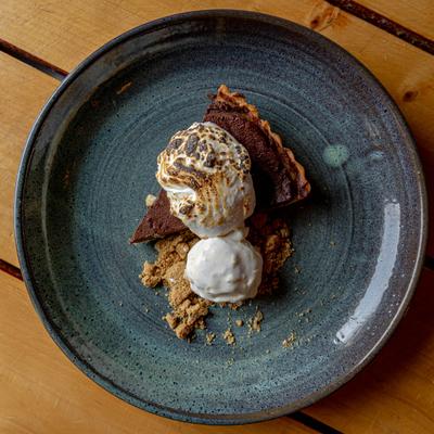 Chocolate tart slice topped with toasted meringue and ice cream, served on graham crumbs.