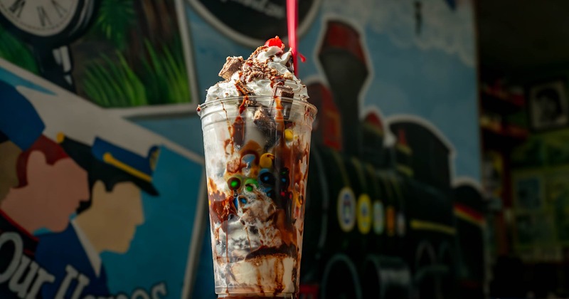 Chocolate candy milkshake with whipped cream, chocolate drizzle, and colorful toppings