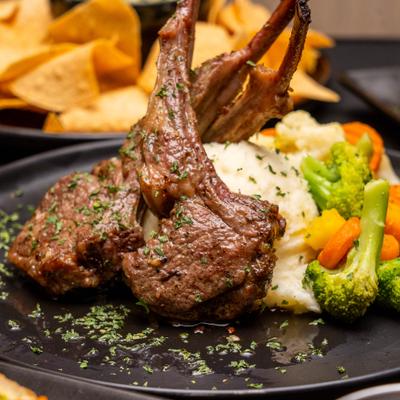 Lamb chops served with sides of mashed potatoes and vegetables.