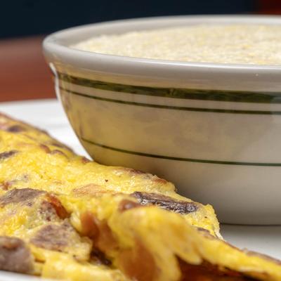 Omelette with sausage, bacon, and ham, served with grits.