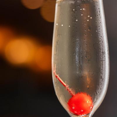 Sparkling wine cocktail in a flute glass, garnished with a cherry.