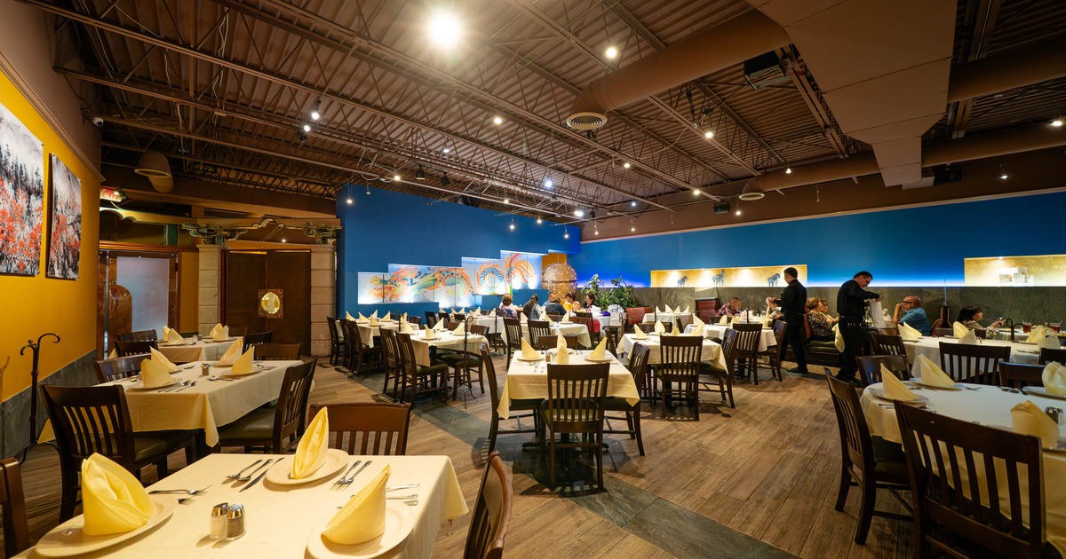 Spacious restaurant interior with cream tablecloths, wooden chairs, and decorative paintings