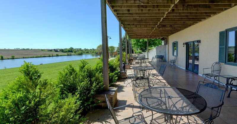 Exterior, outdoor seating area with green shrub fence line, lawn and a view of a lake