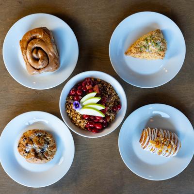 A cinnamon roll, a scone, yogurt parfait, a chocolate chip cookie, and a chocolate croissant.