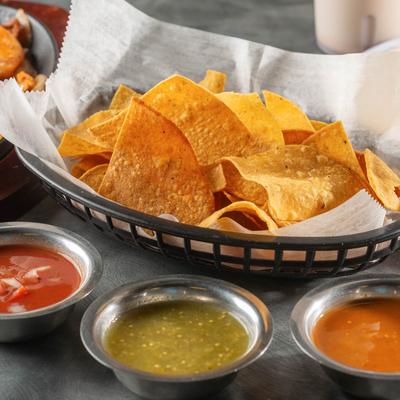 A basket of tortilla chips with assorted salsas.