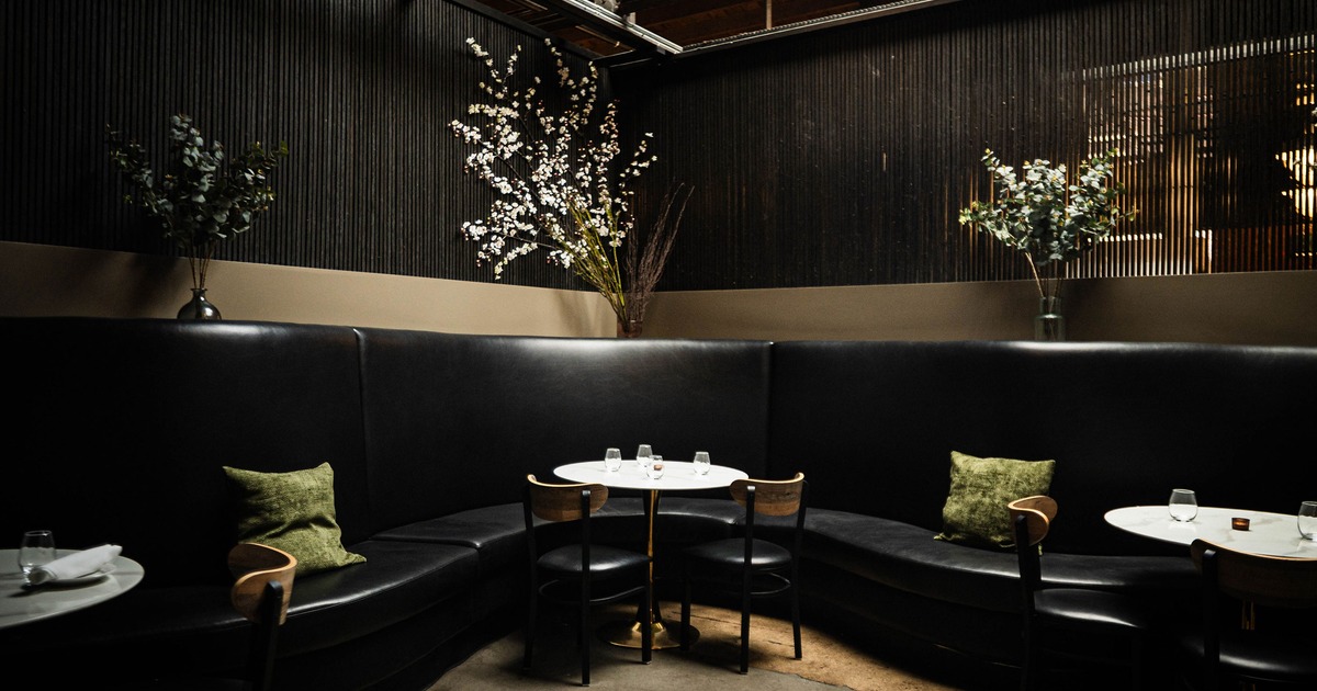 Interior of a modern and intimate, semi-private dining area with curved black leather booth seating