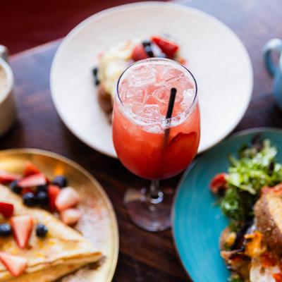 Brunch spread featuring red cocktail in a stemmed glass and various dishes.