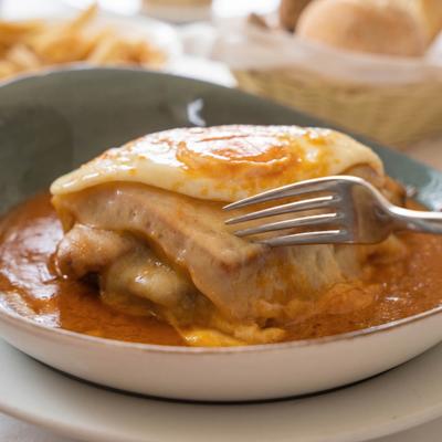 Hearty Portuguese sandwich topped with a fried egg served in a tomato-based sauce.