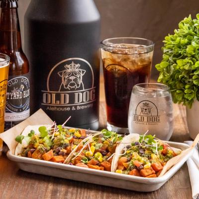 Three tacos served on a plate in front of liquor bottles