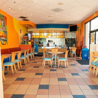 Restaurant interior with tables and chairs, a serving counter, and tropical-themed murals.