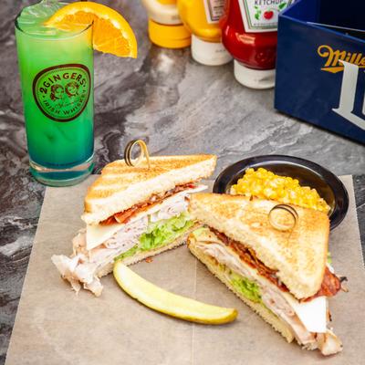 Ham club sandwich with bacon and lettuce, served with corn and a green drink.