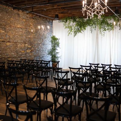 Indoor wedding ceremony space featuring brick walls and black chairs.